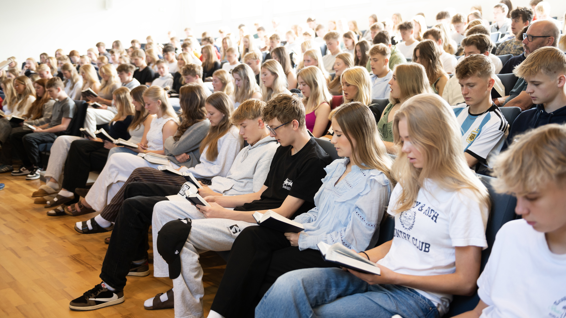 Mange efterskolelever sidder og synger sammen på Gudenaadalens efterskole. 