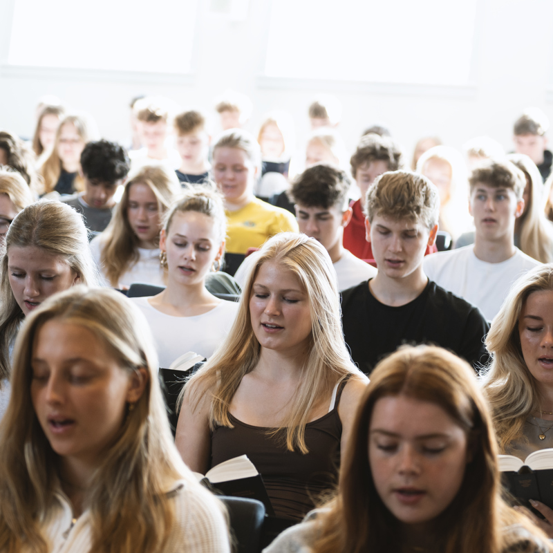 Elever fra Gudenaadalens Efterskole synger sammen i en foredragssal.